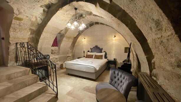 A bedroom with a stone arch, a bed, a chair, a table, and a staircase. - Sevdali Konaklar (Avanos)