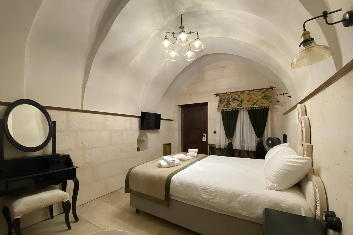 A bedroom with a bed, a desk, a mirror, a television, and a chandelier.
