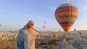 A person observing hot air balloons over a rocky landscape. - Sevdali Konaklar (Avanos)