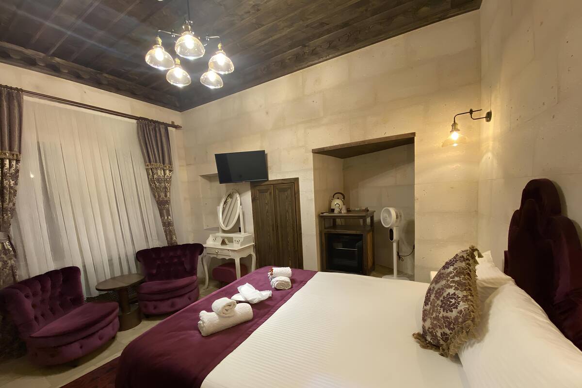 A hotel room with a bed, a vanity with a mirror, a television, a desk, a chair, and a fan.