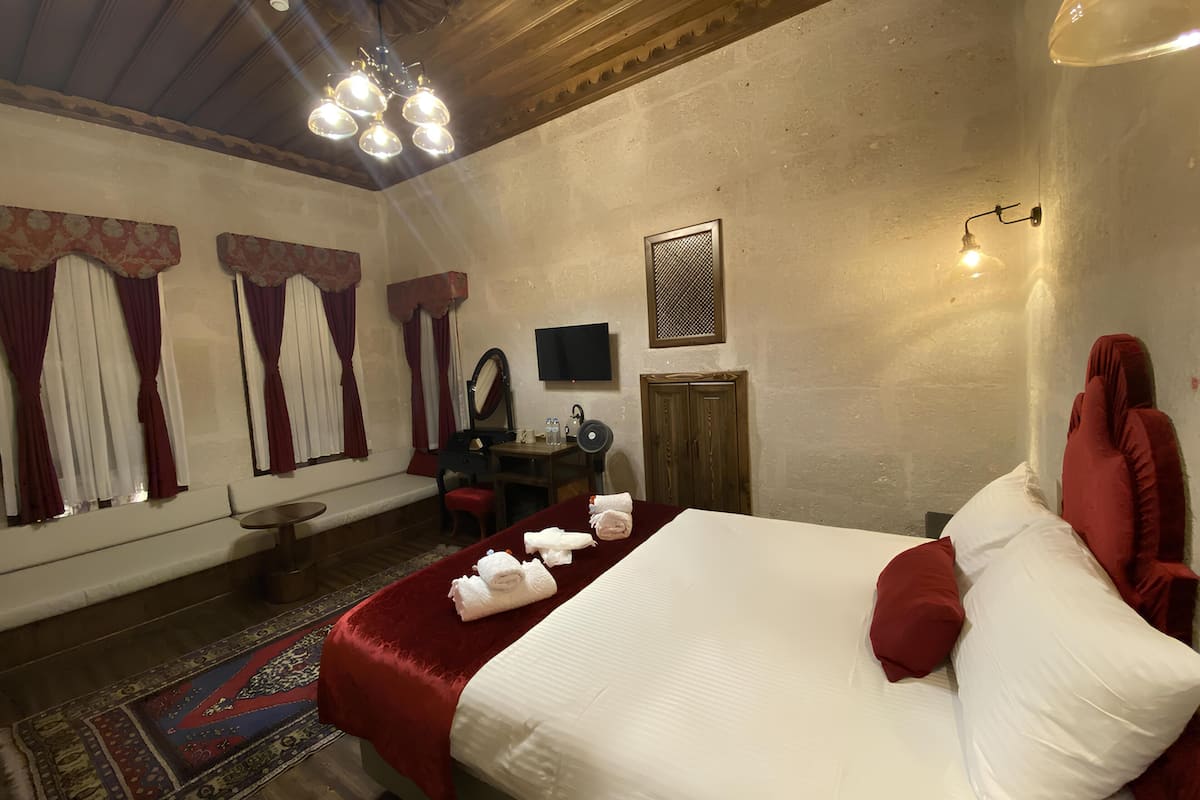 A hotel room with a large bed, a desk with a chair, a television, and a wardrobe.
