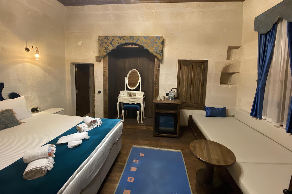 A hotel room with a bed, a desk, a chair, a mirror, and a small table.