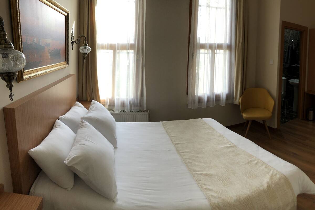 A hotel room with a large bed, a chair, a TV, and a bathroom visible through an open door.