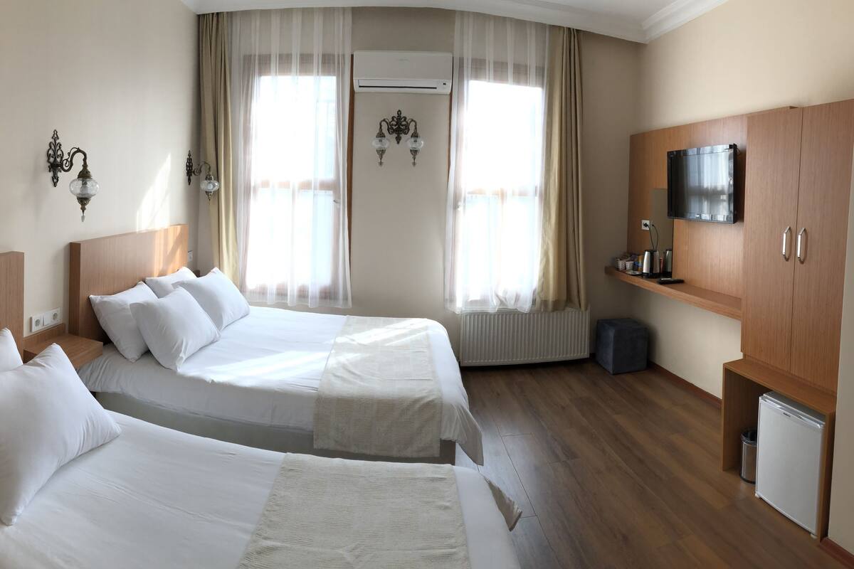 A hotel room with two beds, a TV, a small fridge, and a window with curtains.