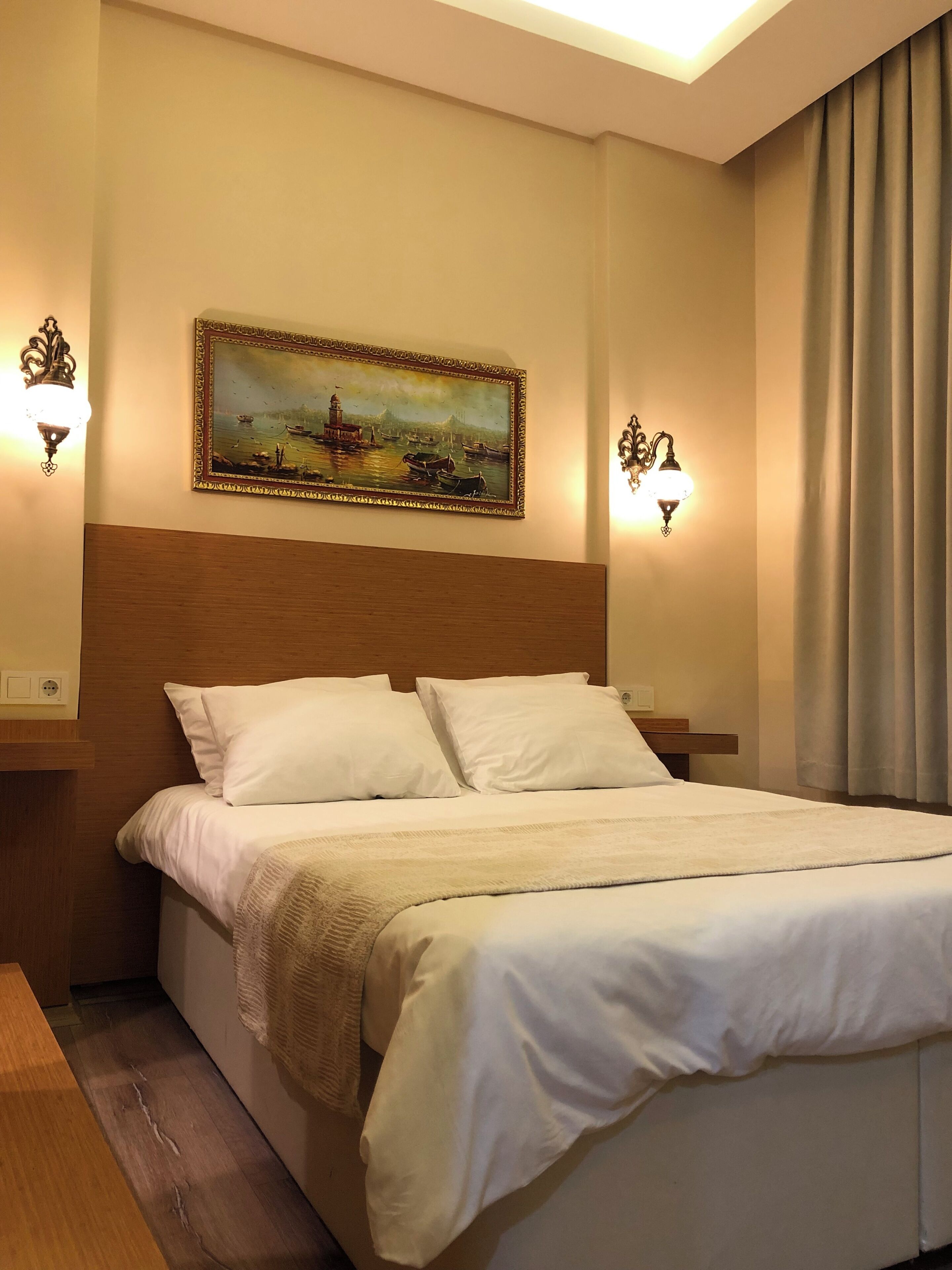 A neatly made bed with white linens, a headboard, and two wall-mounted light fixtures.