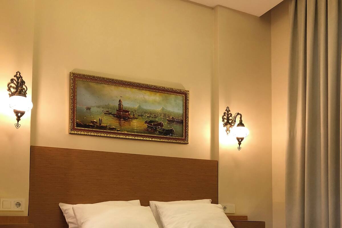 A neatly made bed with white linens, a headboard, and two wall-mounted light fixtures.