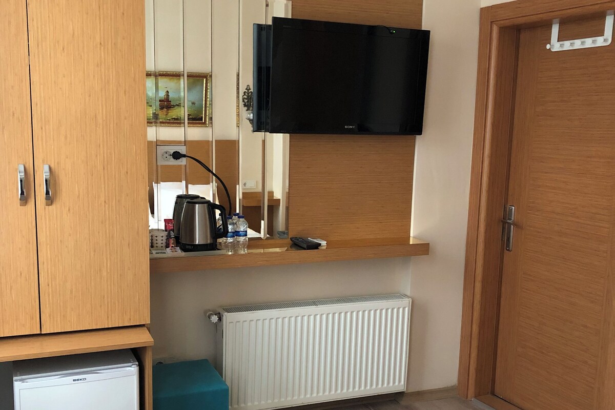 Un dormitorio con cama, armario de madera, refrigerador pequeño, televisor montado en la pared y radiador.