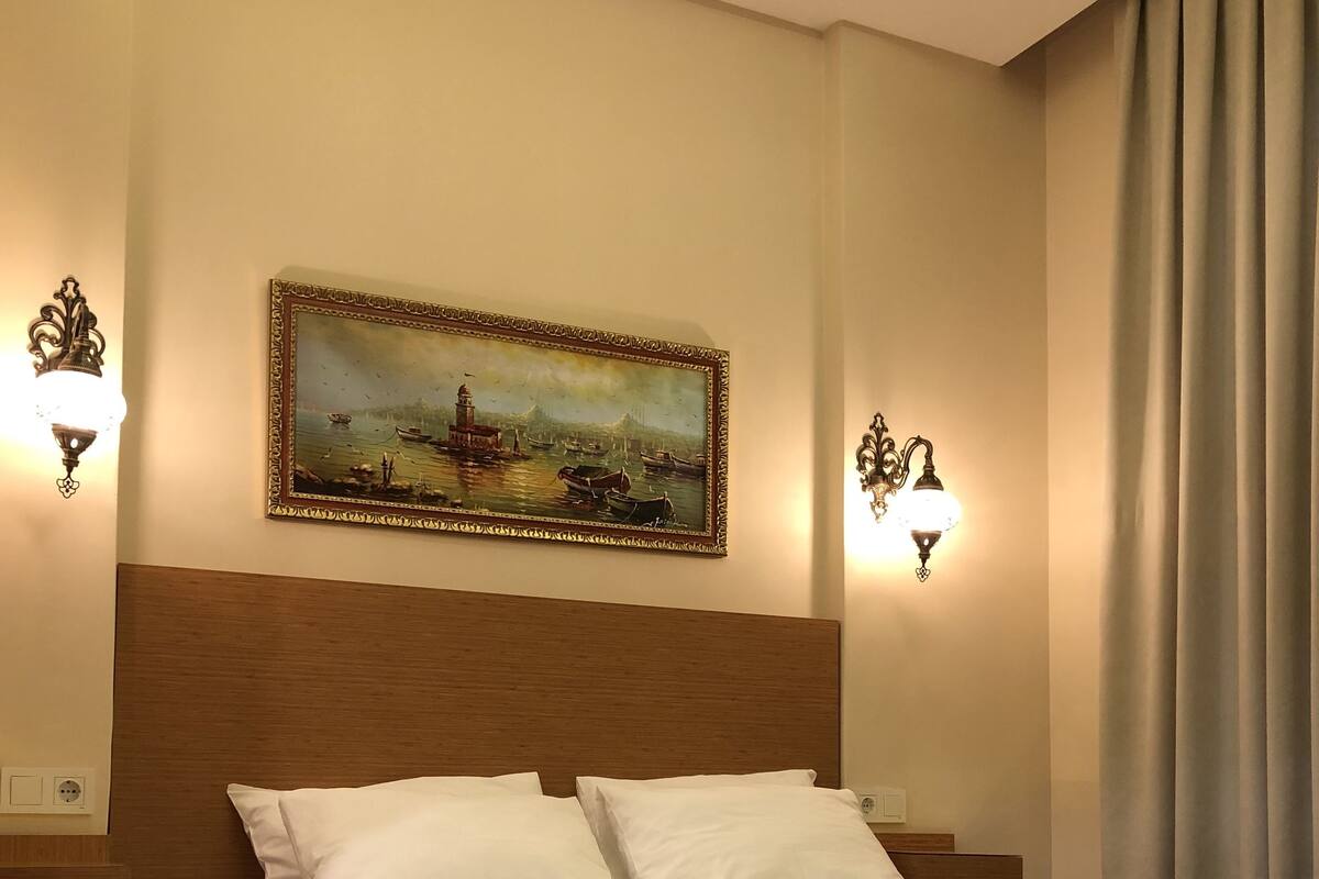 A neatly made bed with white linens, a headboard, and two wall-mounted light fixtures.