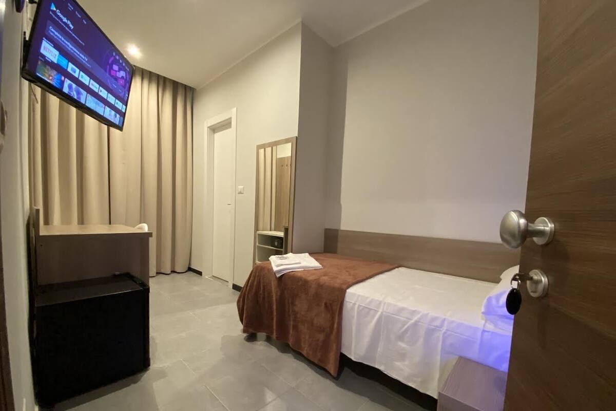 Een hotelkamer met een bed, een tv aan de muur, een houten deur en een klein tafeltje met een stoel.