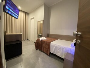 A hotel room with a bed, a TV mounted on the wall, a wooden door, and a small table with a chair. - Hotel Vintage Milano Centrale (Milan)