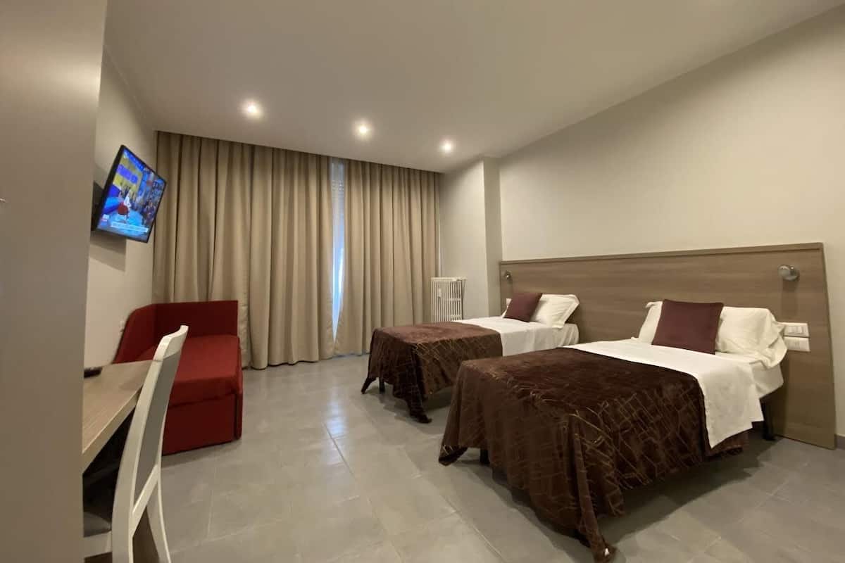 Een hotelkamer met twee bedden, een televisie, een rode bank en een bureau.