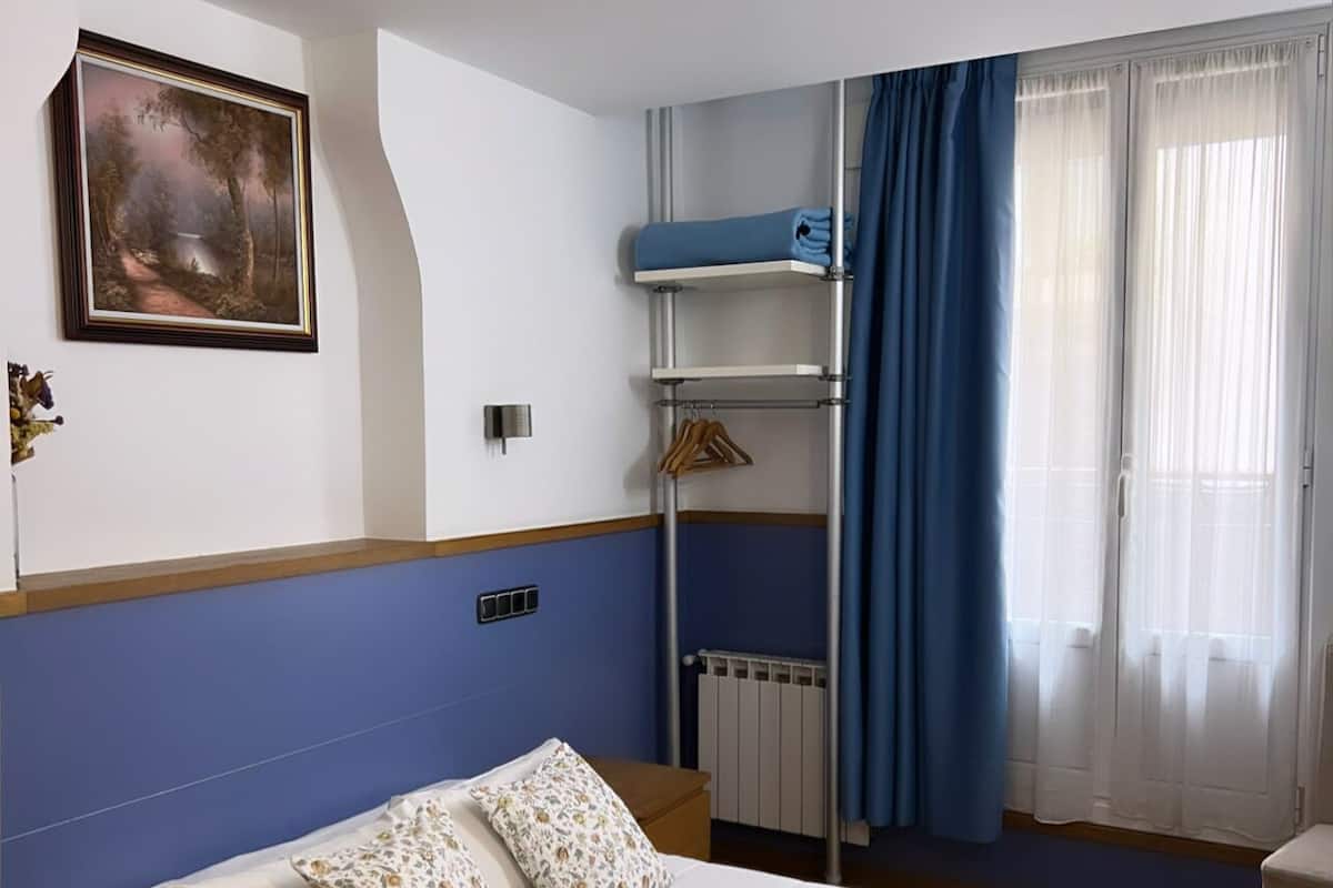 Ein Hotelzimmer mit Bett, einem Gemälde an der Wand, einem Heizkörper und einem Fenster mit Vorhängen.