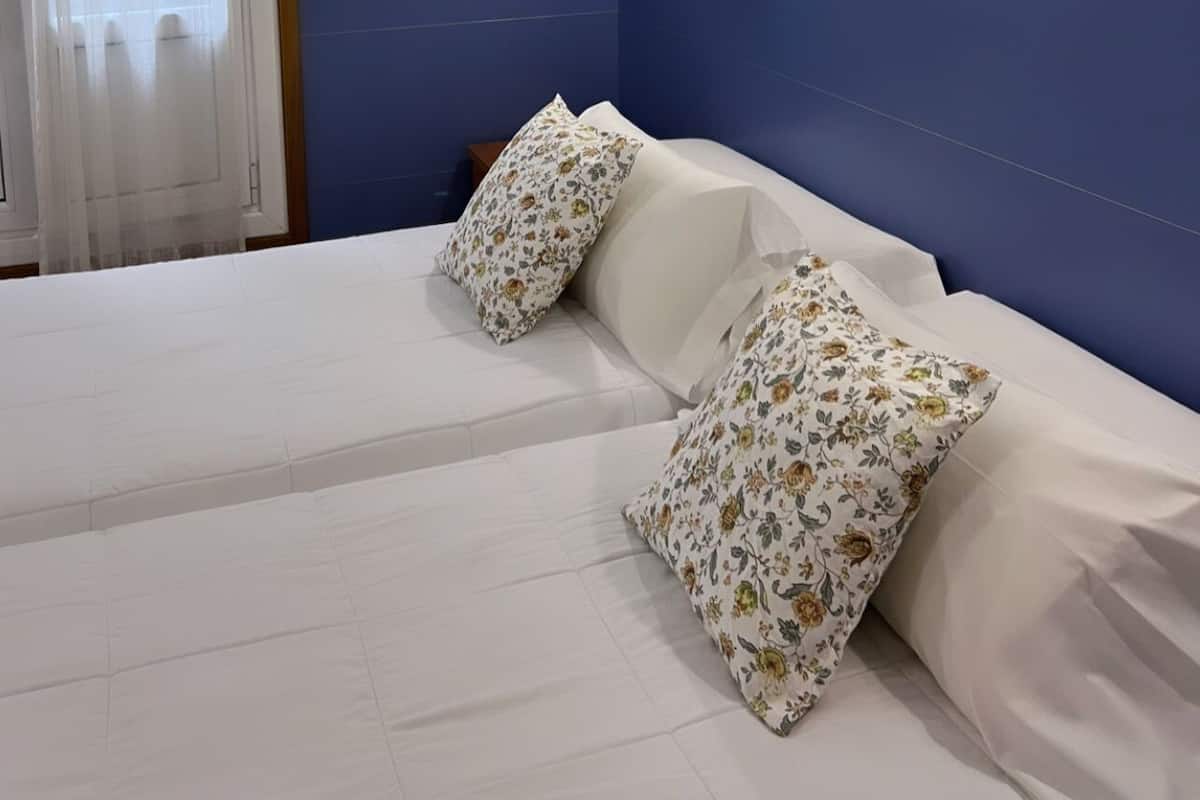 Ein Hotelzimmer mit einem Bett, zwei Kissen, einer Klimaanlage, einem Gemälde und einem Fenster mit Vorhängen.