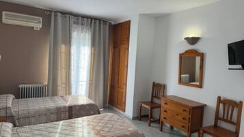 A hotel room with two beds, a wooden dresser, a desk, a chair, a radiator, a TV, and a mirror on the wall.