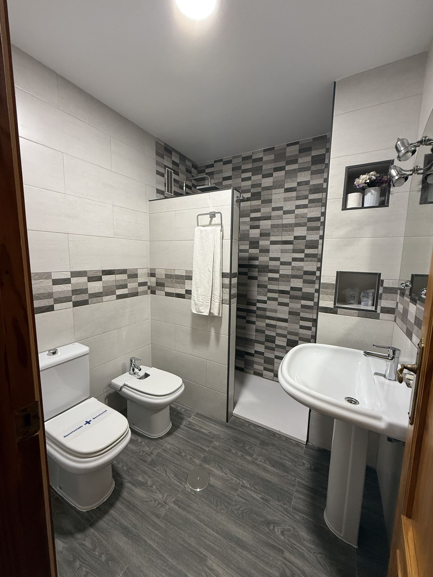 Un baño moderno con ducha, dos inodoros, un lavamanos y un salpicadero de azulejos.