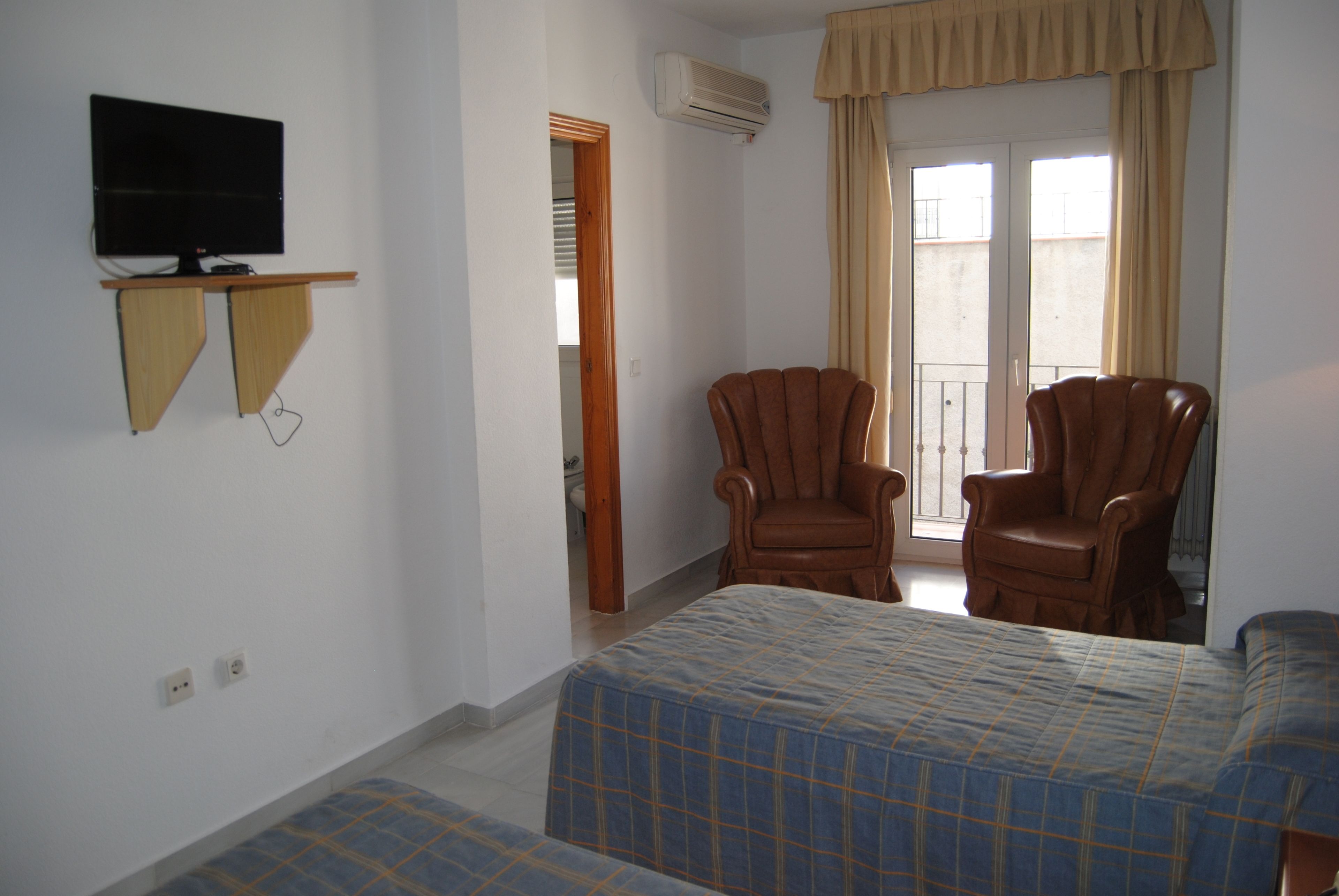 Una habitación de hotel con cama, dos sillones, televisor y ventana con cortinas.