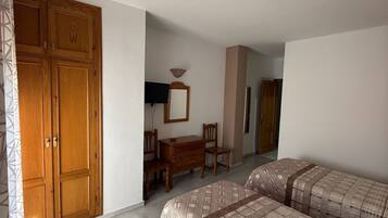 A bedroom with two beds, a wooden wardrobe, a desk with a chair, and a mirror on the wall.