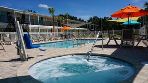 A pool area with lounge chairs, umbrellas, and a hot tub.