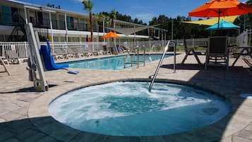 Relax by the pool with a hot tub at the center, surrounded by lounge chairs and umbrellas.