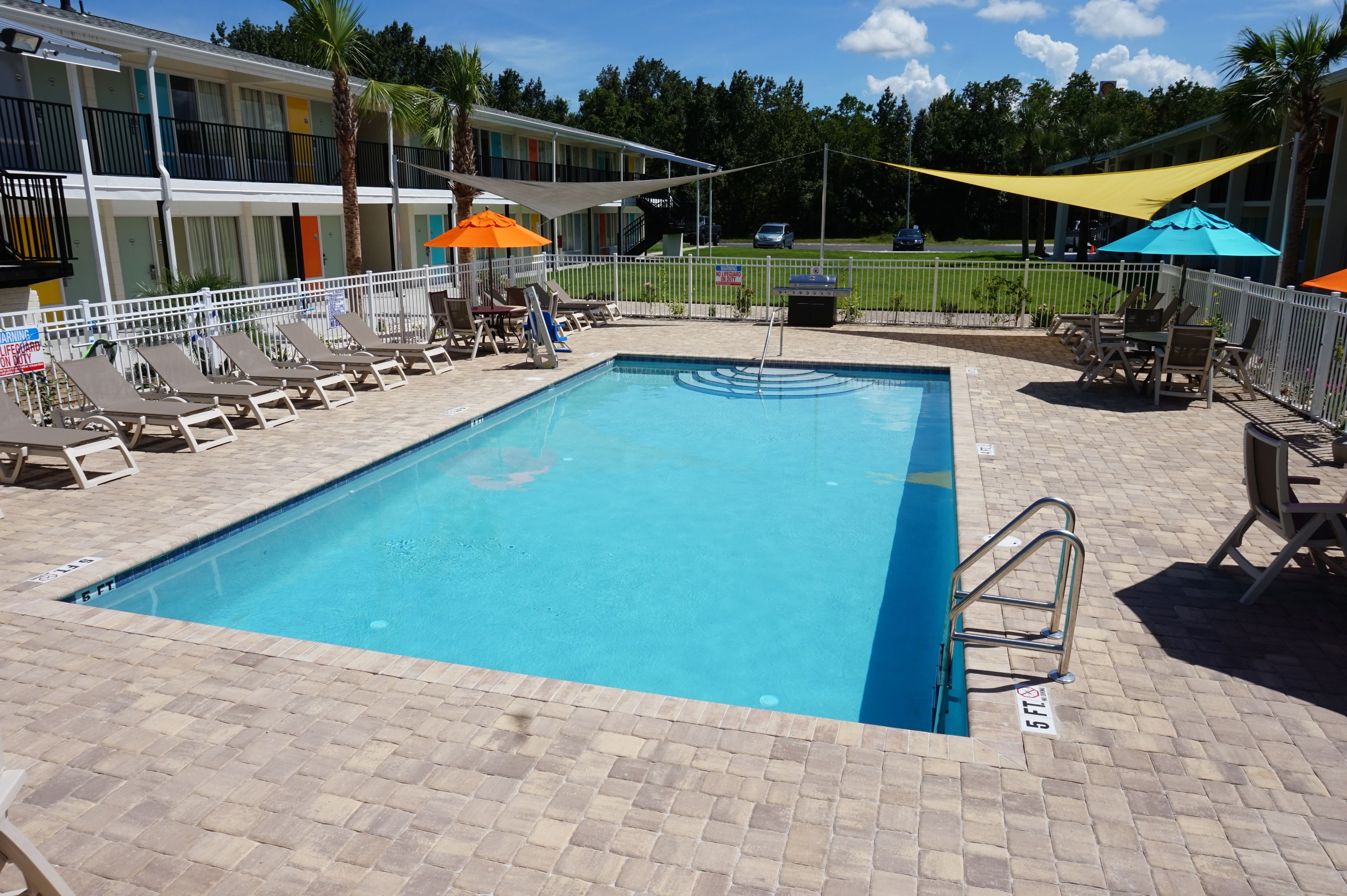 A rectangular pool with a ladder on one side, surrounded by lounge chairs and umbrellas.