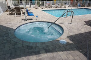 Una vasca idromassaggio con scaletta metallica, circondata da poltrone relax e una piscina.