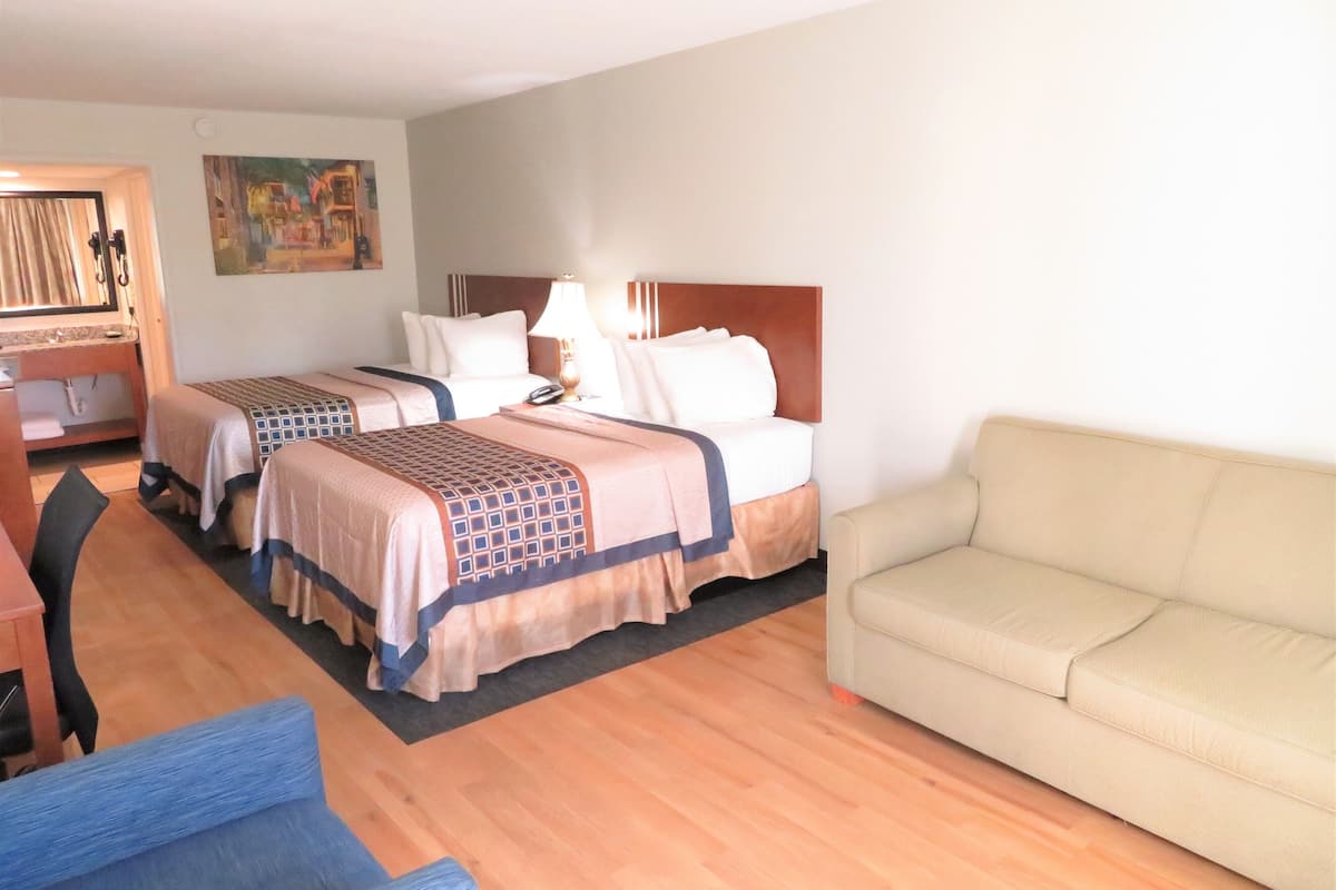A hotel room with two beds, a sofa, a desk, and a chair.