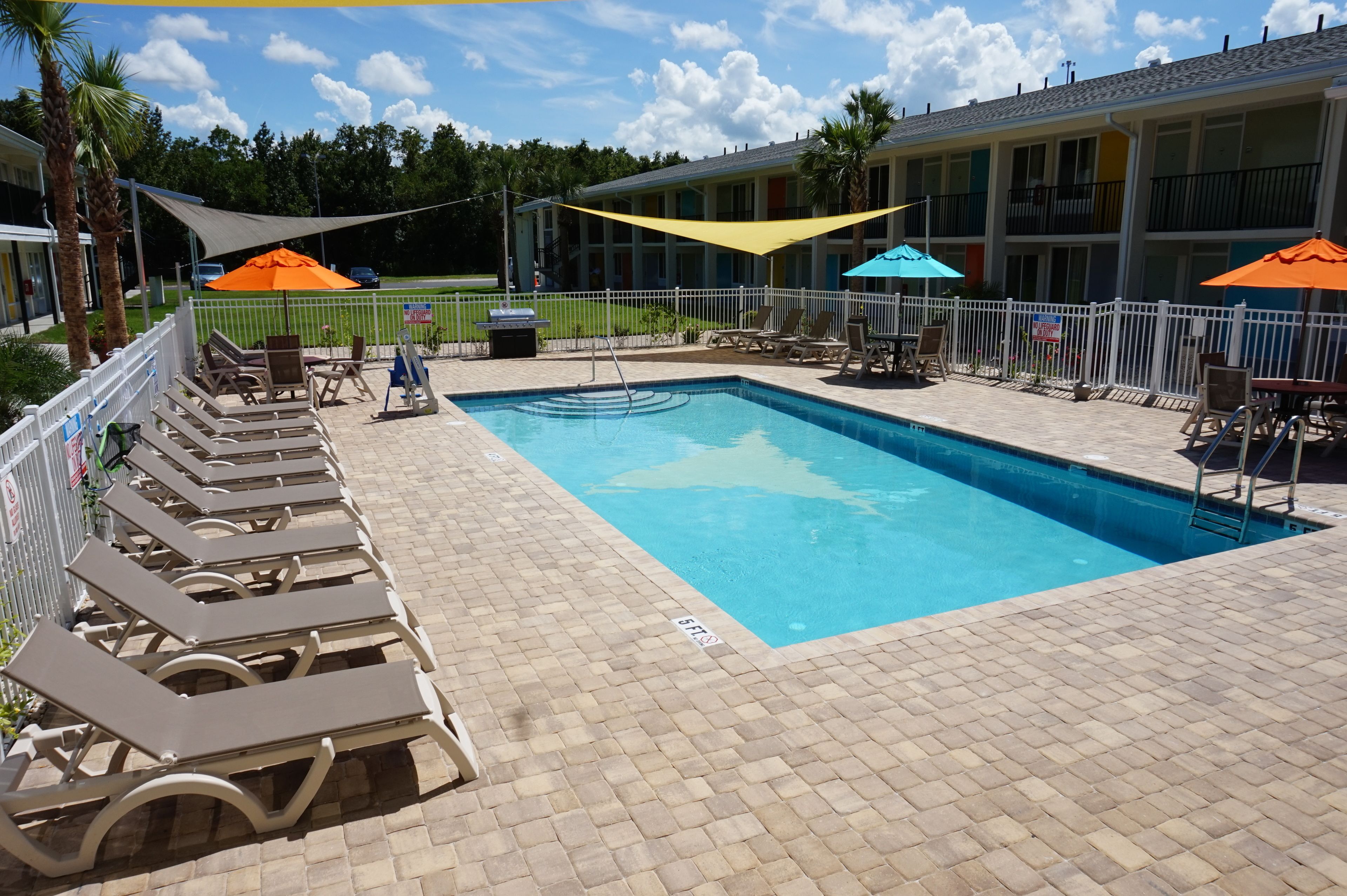 A pool area with lounge chairs and umbrellas, surrounded by a white fence.