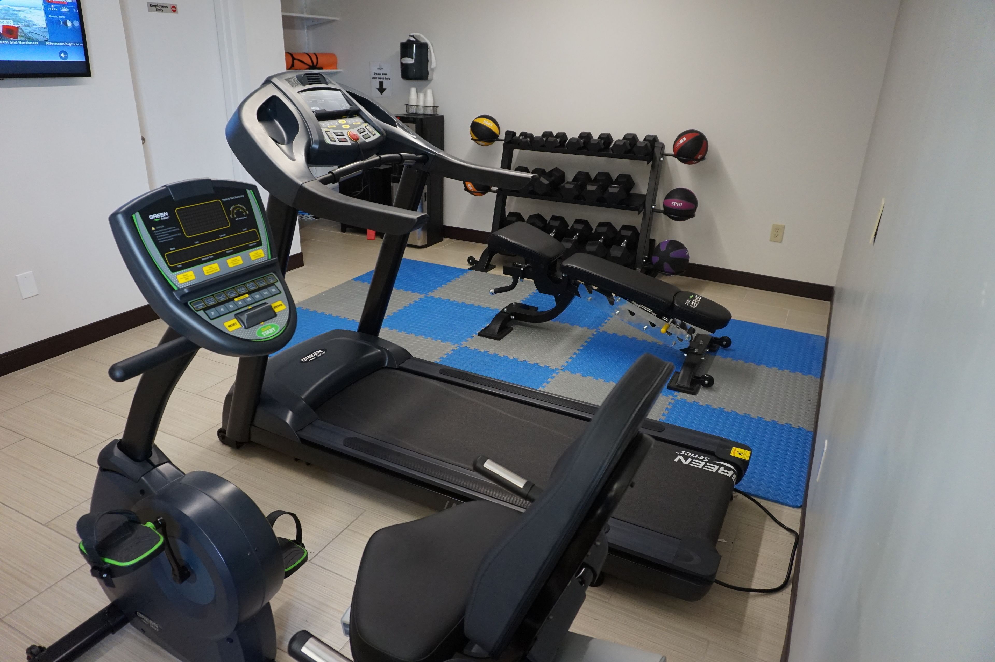 Un gimnasio con cinta de correr, elíptica y mancuernas.