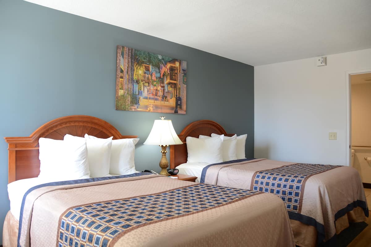 A hotel room with two beds, a painting on the wall, and a lamp.