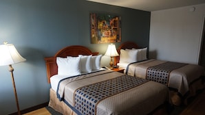 Habitación de hotel con dos camas, un cuadro en la pared, una lámpara y suelo de madera.