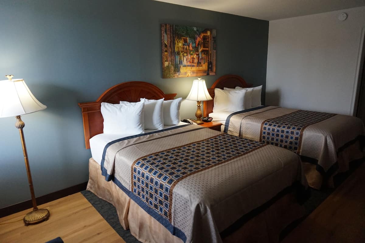 A hotel room with two beds, a painting on the wall, a lamp, and a wooden floor.