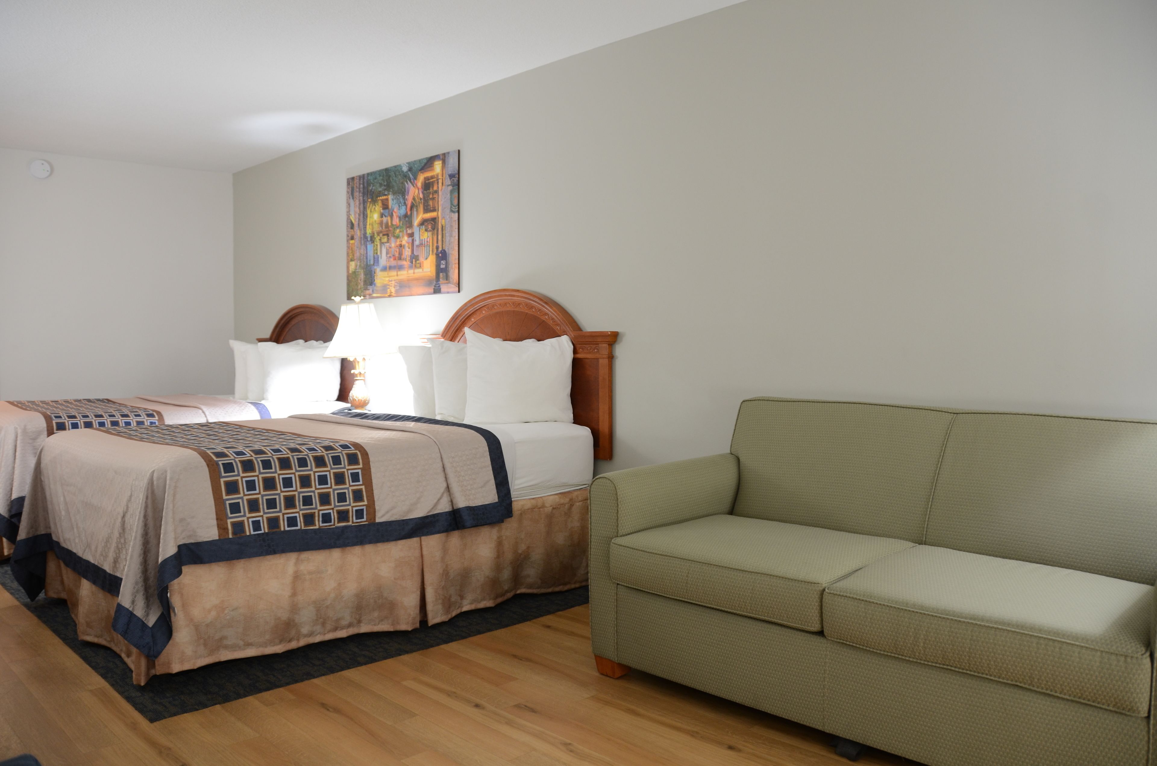 Ein Hotelzimmer mit zwei Betten, einem grünen Sofa und einem Gemälde an der Wand.