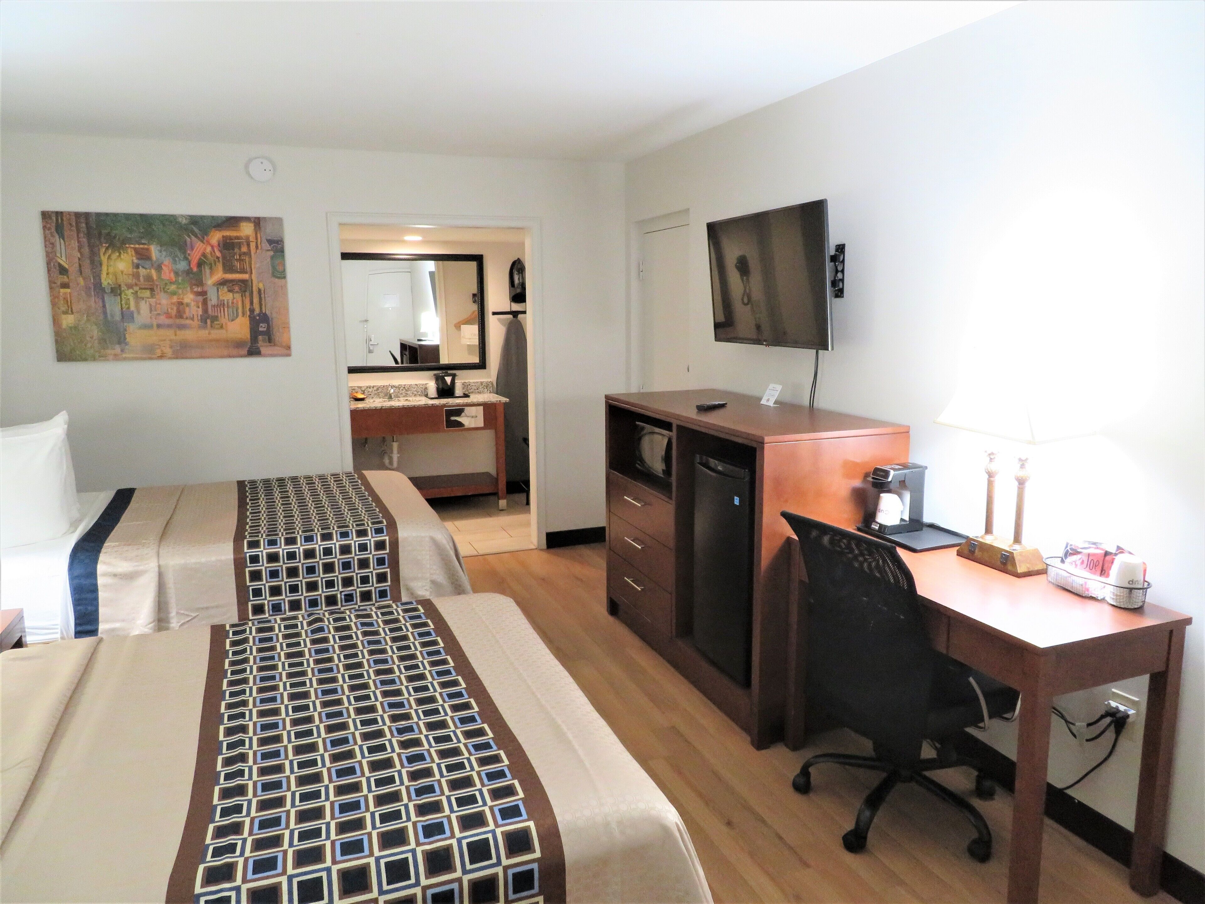 Une chambre d’hôtel avec deux lits, un bureau, une chaise, une télévision et une salle de bain visible à travers une porte ouverte.