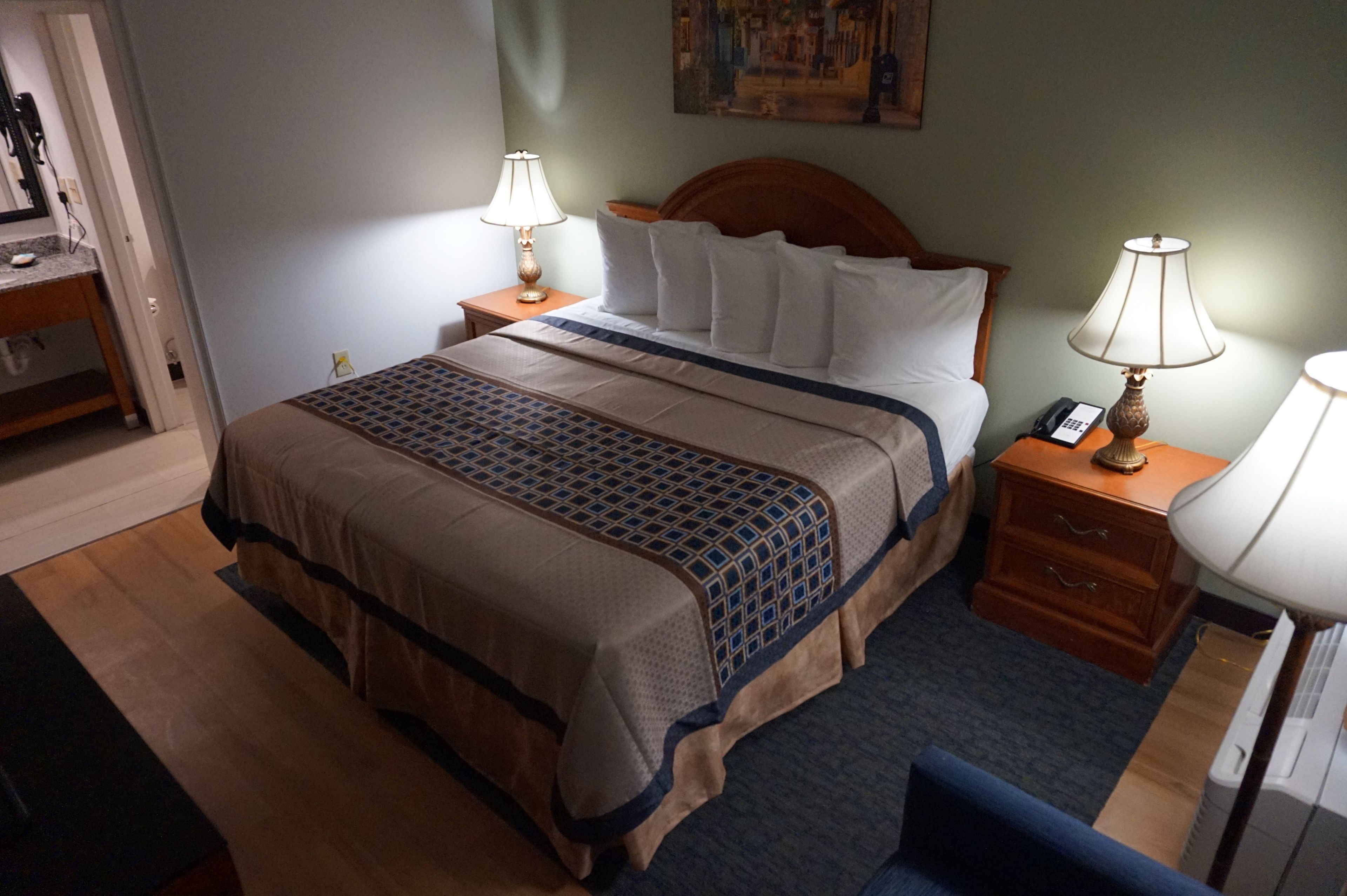 Een hotelkamer met een bed, twee nachtkastjes met lampen, een houten hoofdeinde en een schilderij aan de muur.