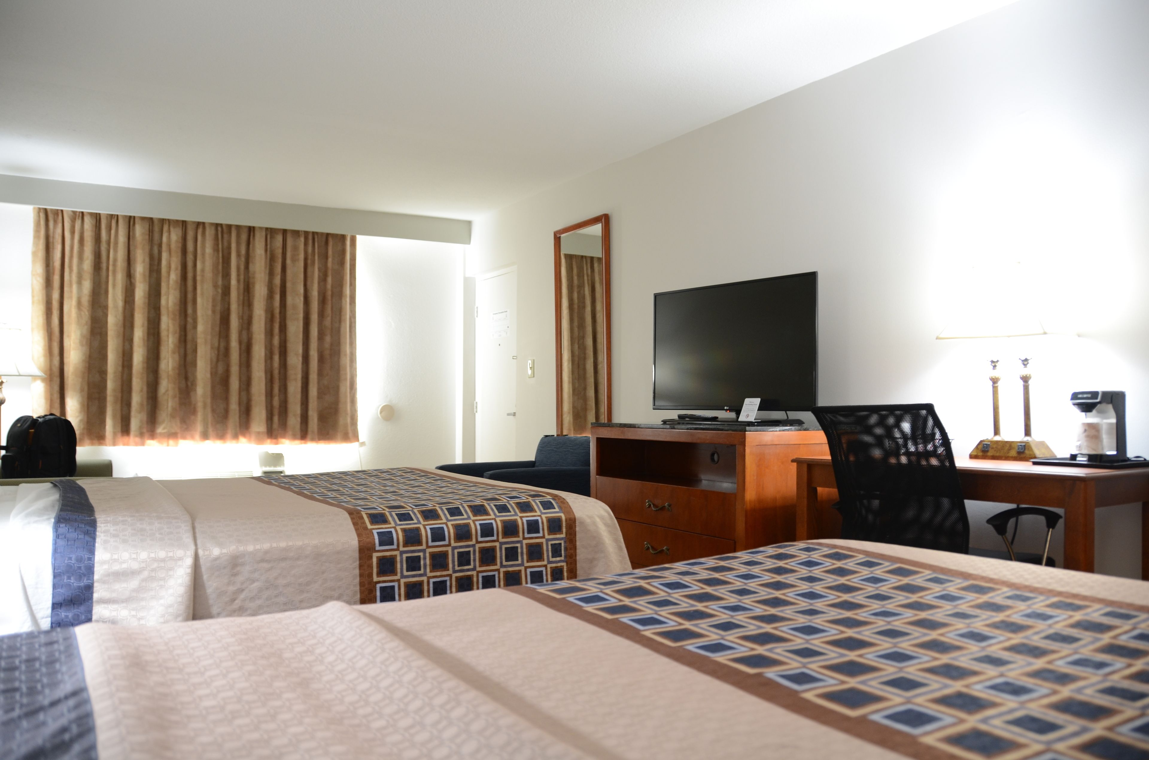 A hotel room with two beds, a desk, a chair, a television, and a window with curtains.