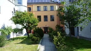Um pátio com um caminho, cercado por edifícios com painéis solares no telhado e vegetação.