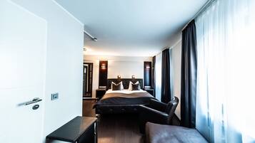 A modern hotel room with a bed, a desk, and a chair. There is a door and a window with curtains.