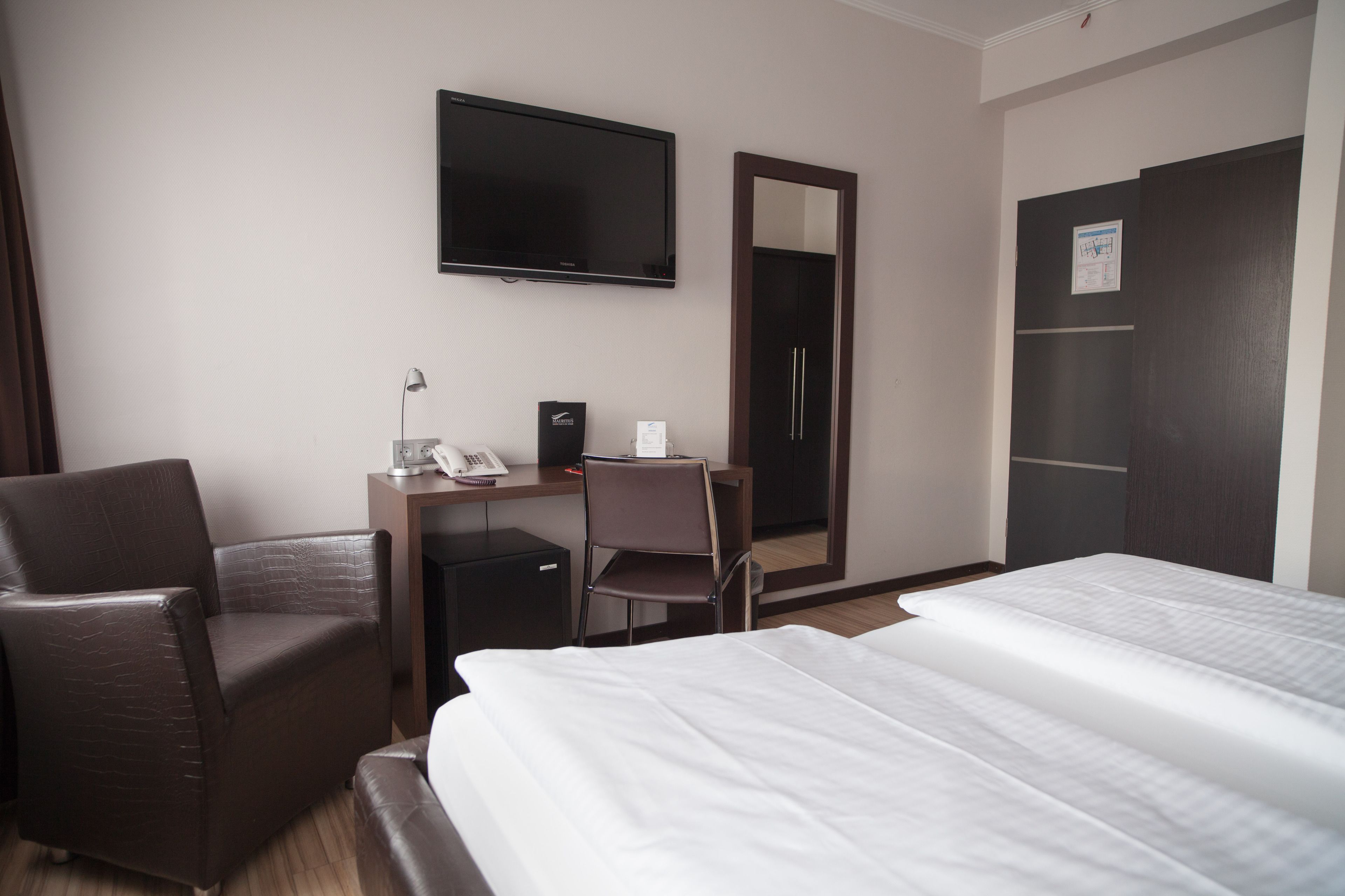 Ein Hotelzimmer mit Bett, Schreibtisch mit Stuhl, Fernseher und Kleiderschrank.