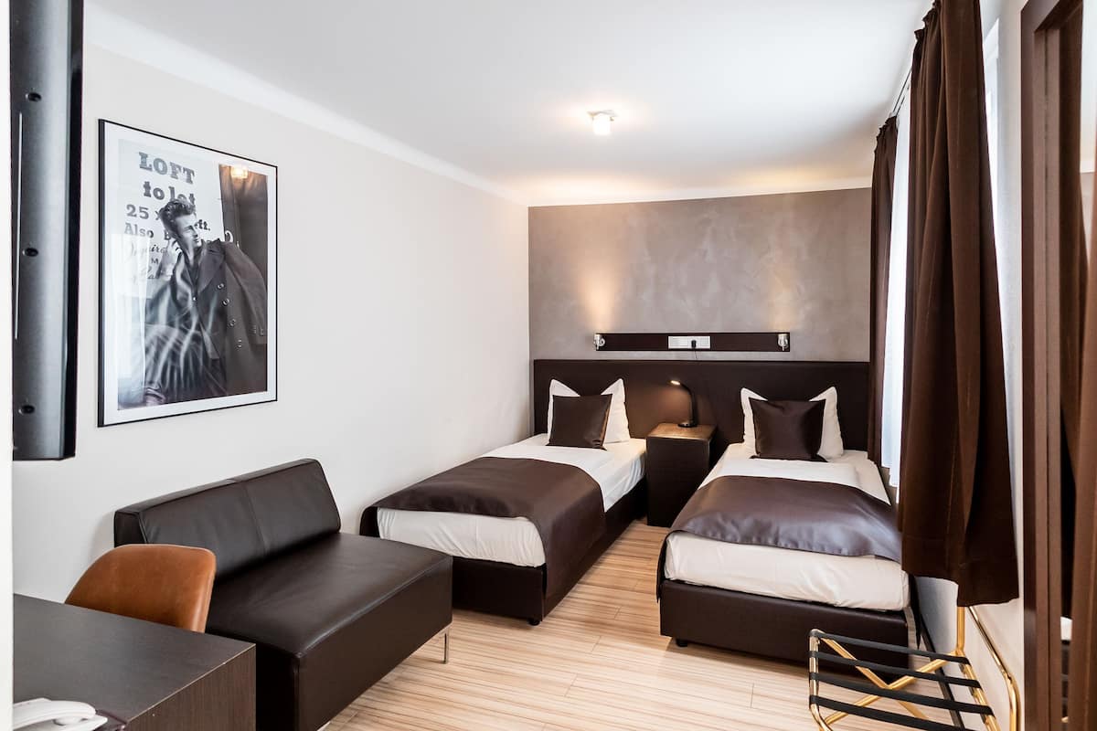 Une chambre d’hôtel avec deux lits, un bureau, un canapé et une affiche au mur.