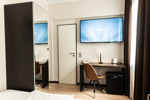 Habitación de hotel con cama, escritorio con computadora, televisión, teléfono y refrigerador pequeño.