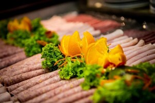 Un bufé con comidas dispuestas de forma ordenada, incluyendo fiambres y adornado con lechuga y rodajas de naranja.