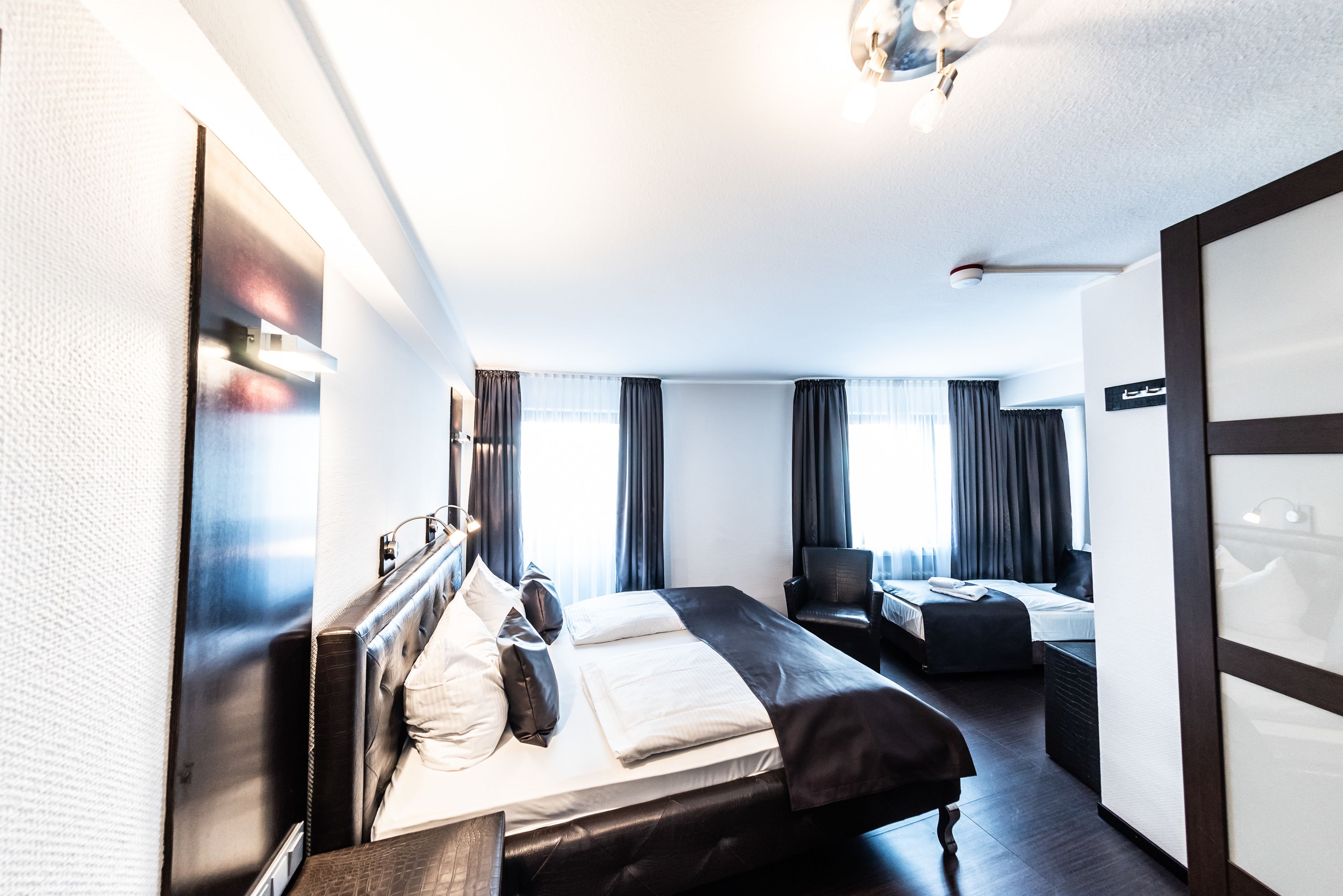 Ein Hotelzimmer mit einem großen Bett, einem Schreibtisch und einem Stuhl. Vor den Fenstern hängen Vorhänge und an der Wand befindet sich ein Schild.