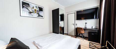 A hotel room with a bed, a desk, a chair, a television, and a mirror.
