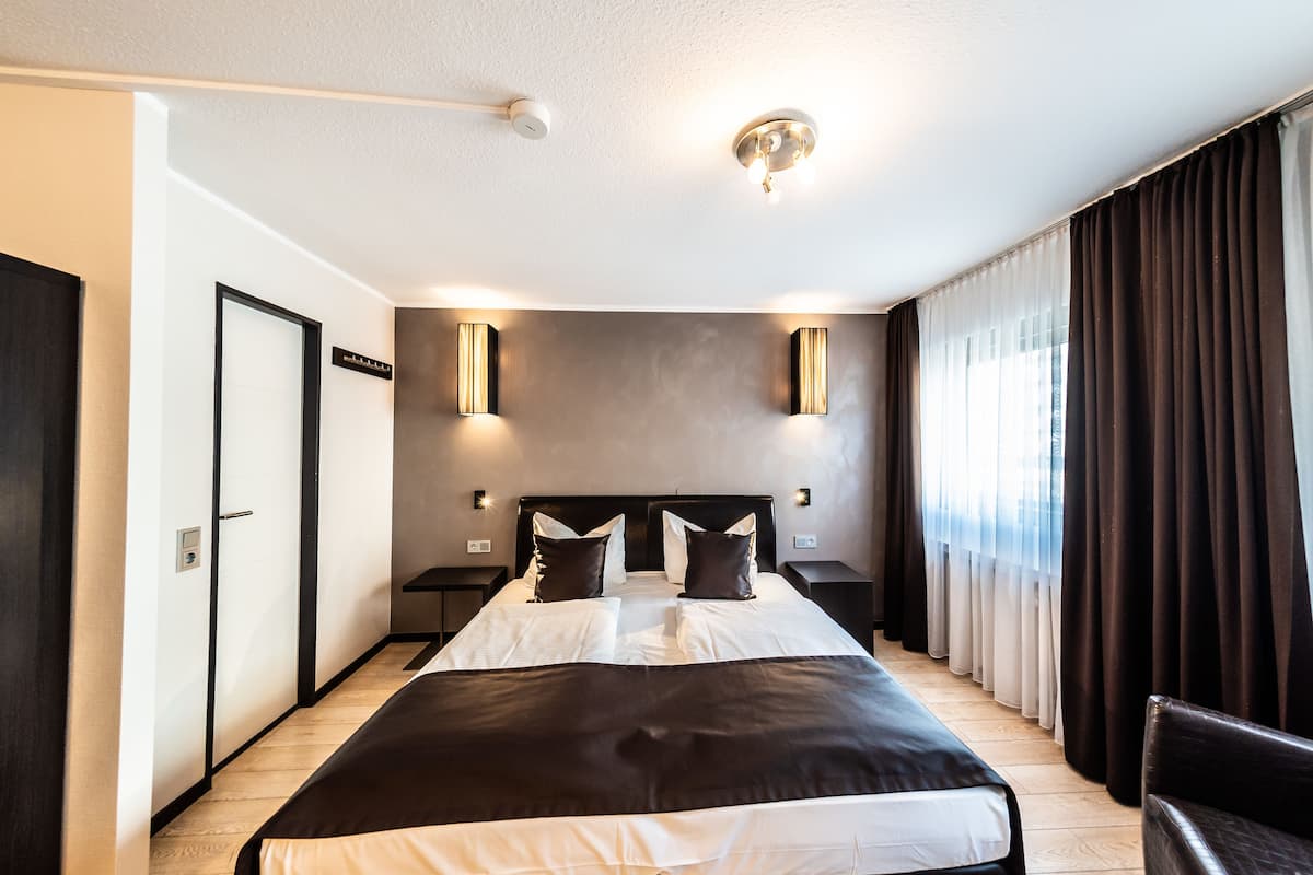 Une chambre d’hôtel moderne avec un grand lit, des rideaux foncés et des luminaires fixés au mur.