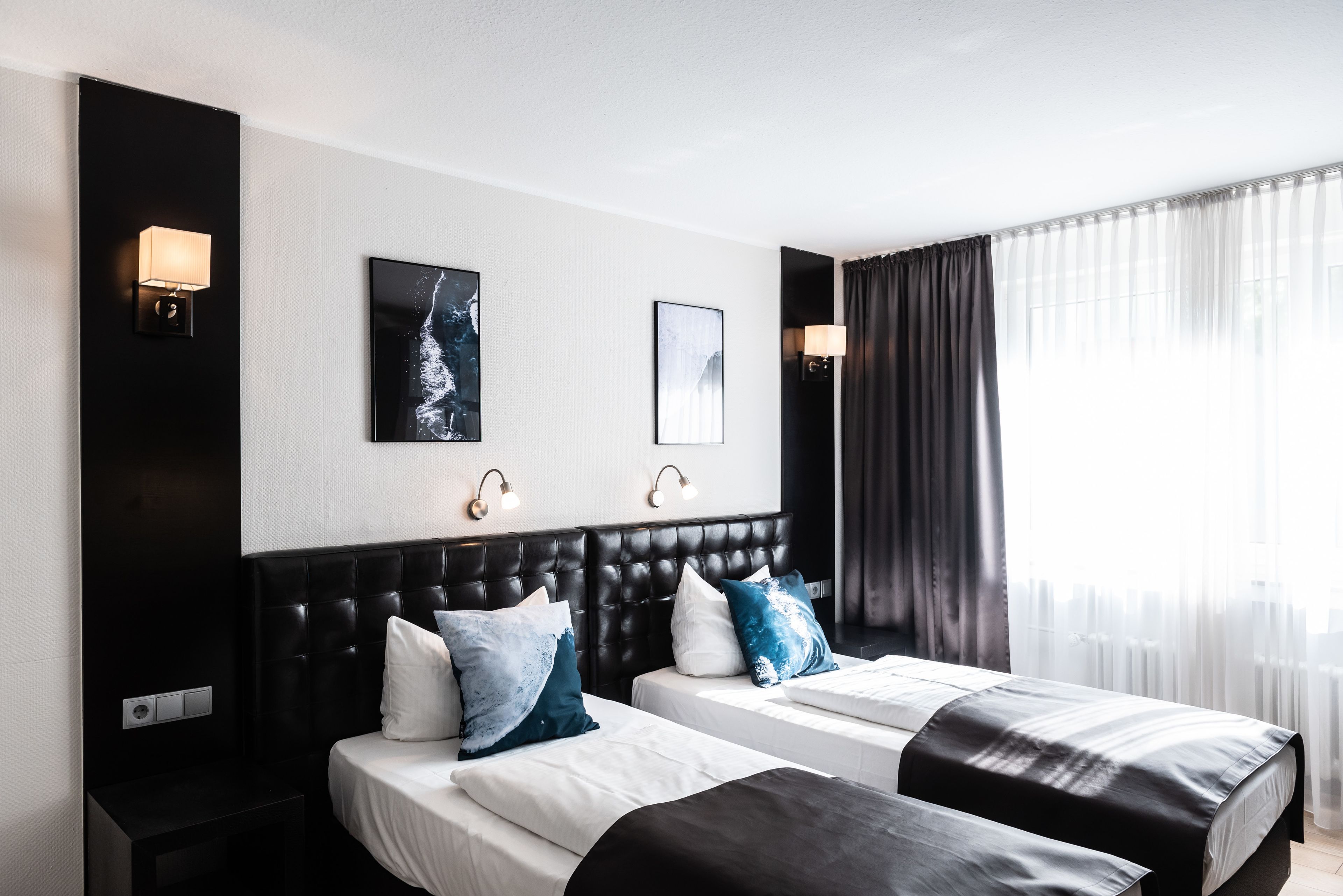 Ein Hotelzimmer mit zwei Betten, einem schwarzen Kopfteil und zwei Wandleuchten.