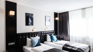 Ein Hotelzimmer mit zwei Betten, einem schwarzen Kopfteil und zwei Wandleuchten.
