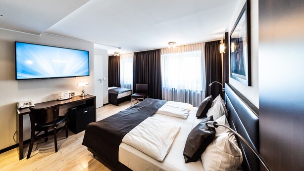Una habitación de hotel con cama, escritorio, silla, televisor y cortinas.