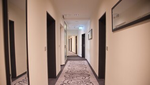 Un pasillo de hotel con alfombra estampada, puertas a ambos lados y un espejo en la pared derecha.