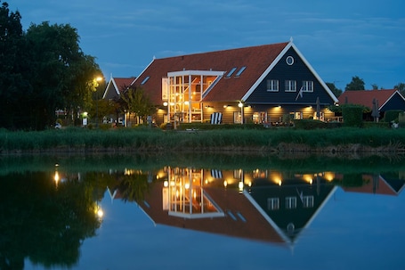 A traditional building with a sloped roof, large windows, and a reflection in the water.