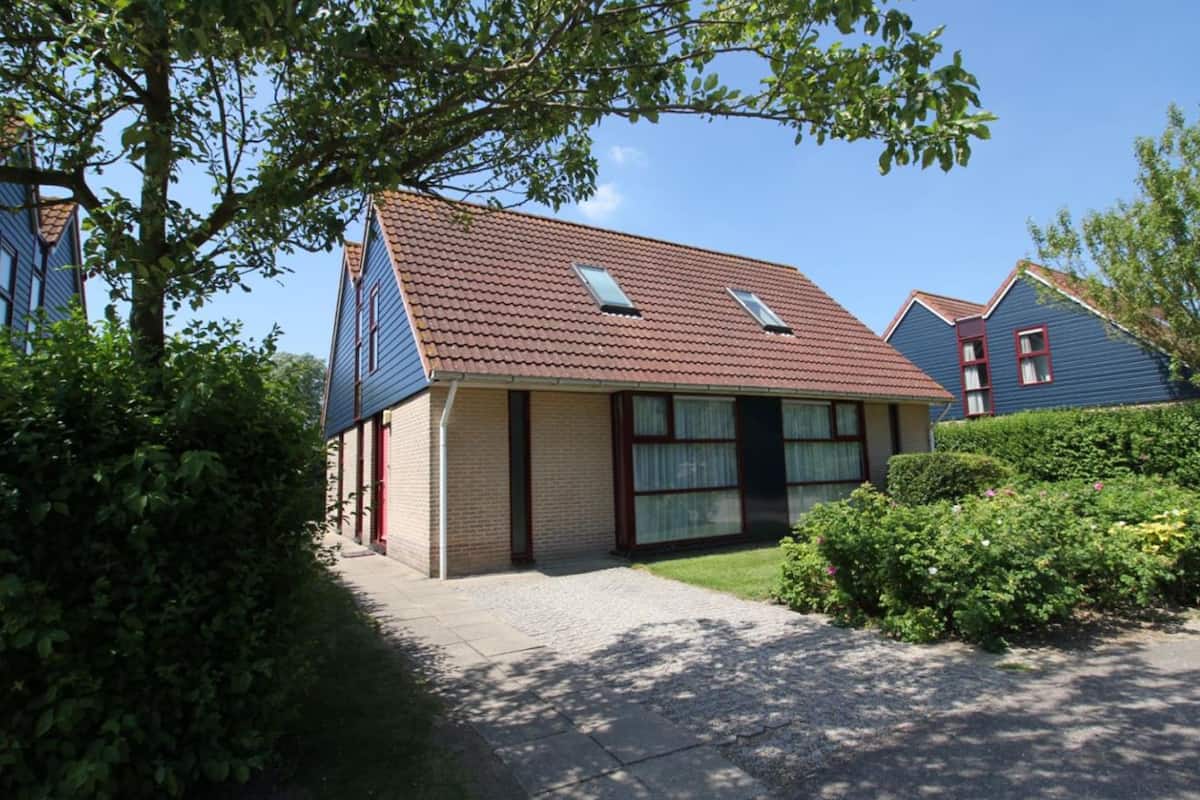Une maison d’habitation avec un toit en pente, un porche à l’avant et une pelouse bien entretenue.